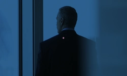 A man in a suit stands with his back to the camera, looking out of a large window. The image has a blue tint and a business-like atmosphere.