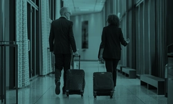 A soft-lit hallway, where a man and woman in suits walk, luggage in tow. Windows line the scene, adding a professional touch to this hotel or office snapshot.
