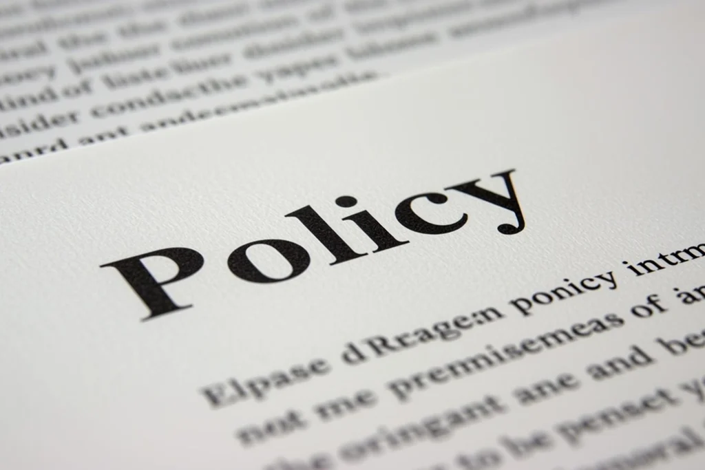 Close-up of a printed document with the word Policy in large, bold letters at the top. The rest of the text below appears blurred and partially visible.