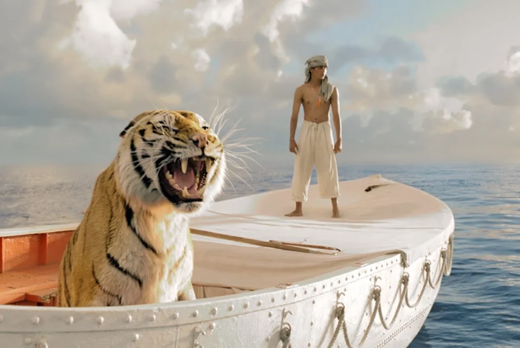 A young man stands on a lifeboat at sea, looking into the distance, while a tiger with its mouth open sits at the front of the boat. The sky is cloudy and the ocean is calm.