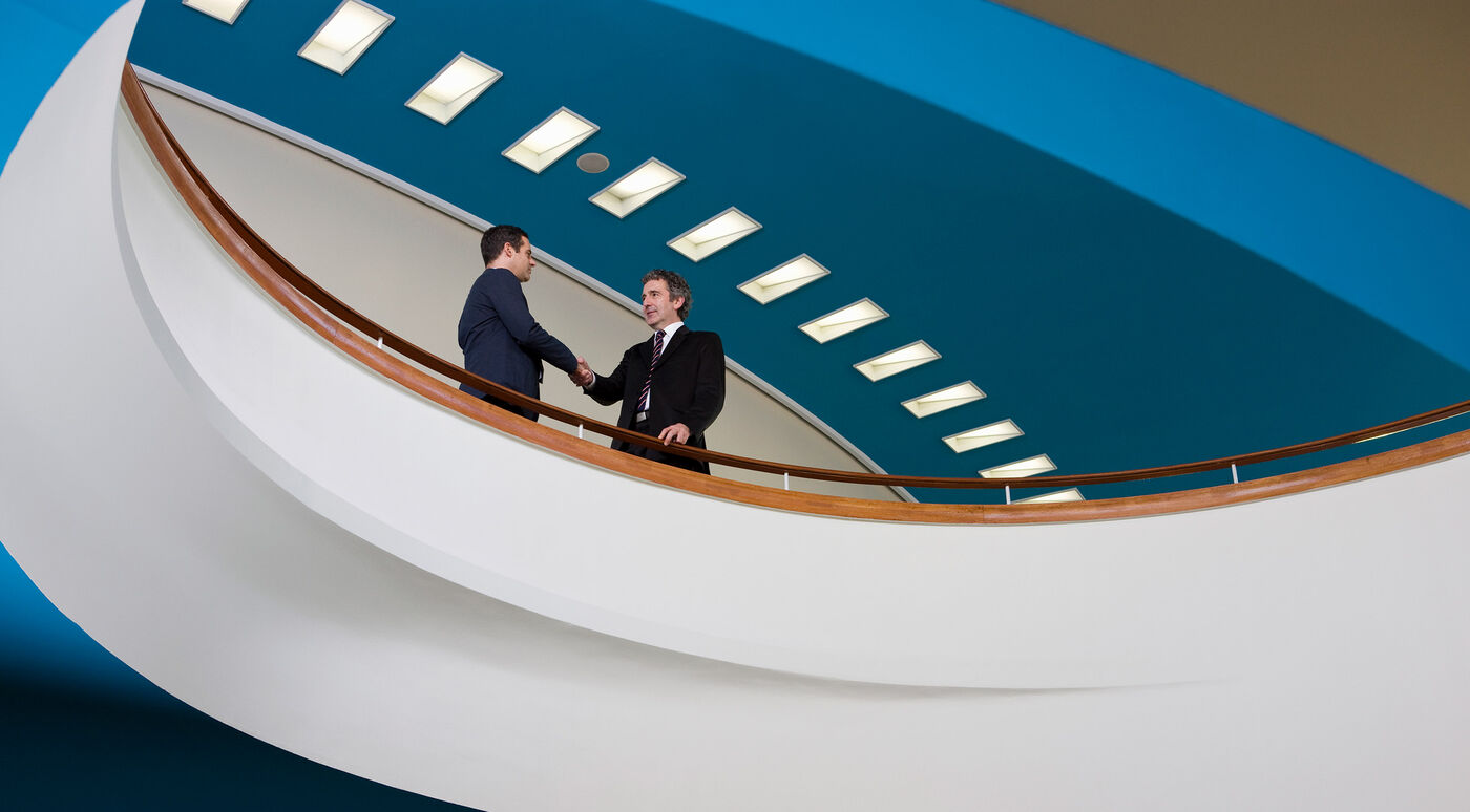 Two executives shake hands on a staircase