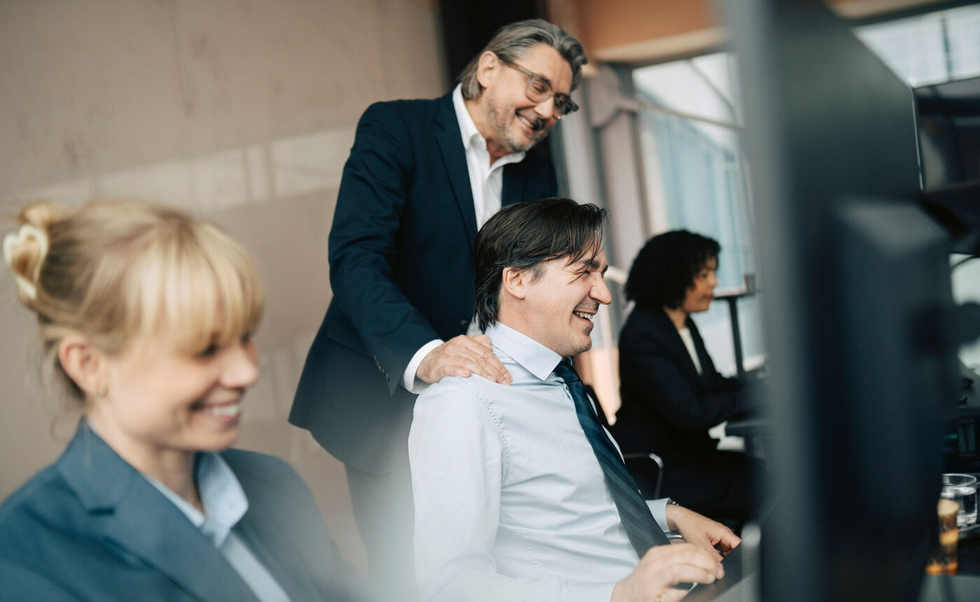 A senior advisor laughs with a colleague at his desk